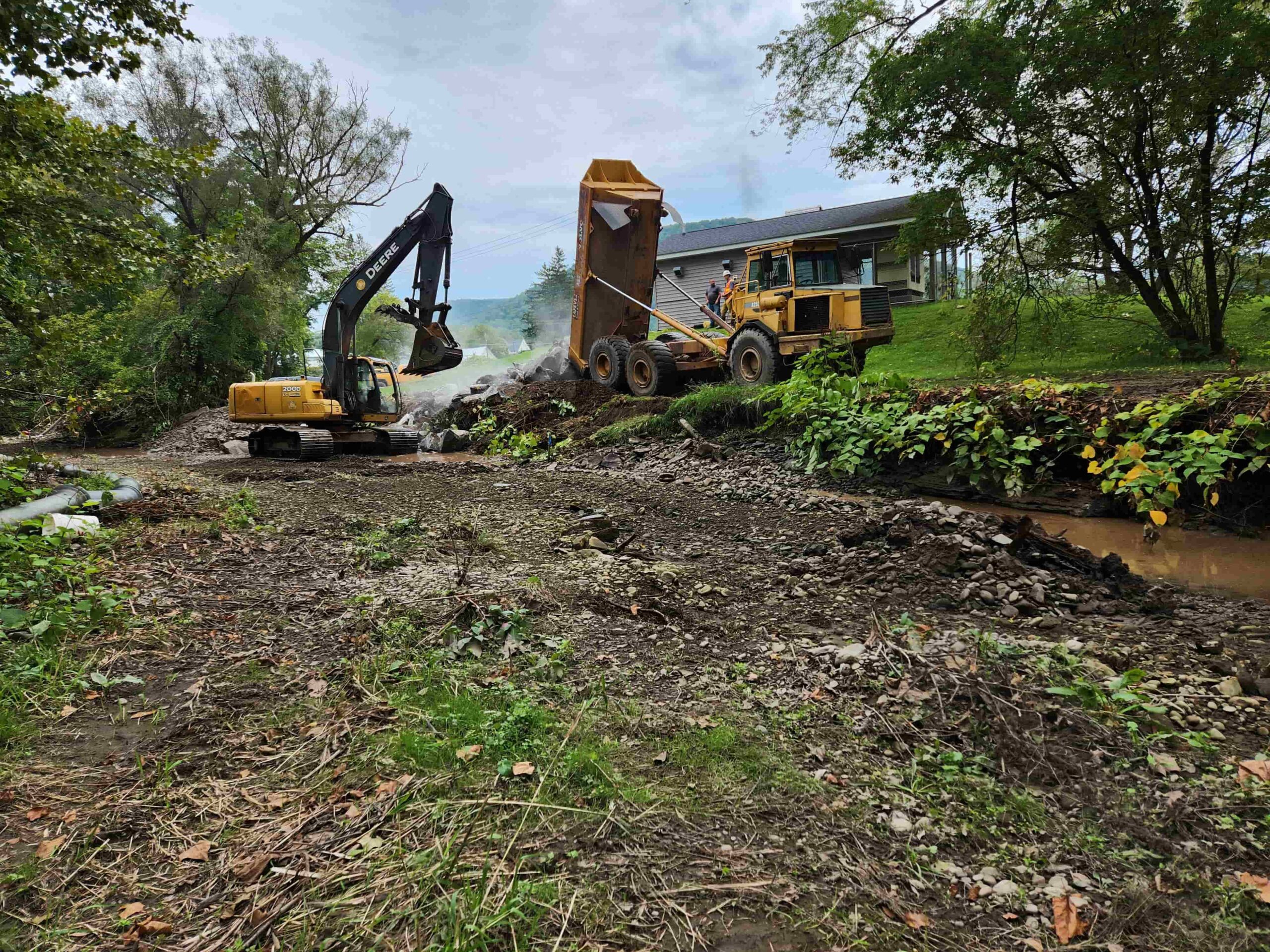 Beginning of Walton Village's West Brook stream well bank stabilization project remediation showing large excavator and dump truck reconfiguring streambank soil.