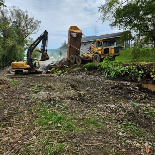 Beginning of Walton Village's West Brook stream well bank stabilization project remediation showing large excavator and dump truck reconfiguring streambank soil.