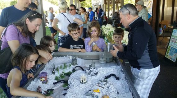 Image description: Children gathered around stream demonstration table with stream program staff member discussing streams.