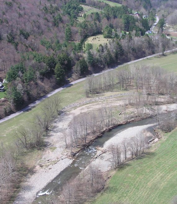 Drone view of river valley with mountains rising up on left side.